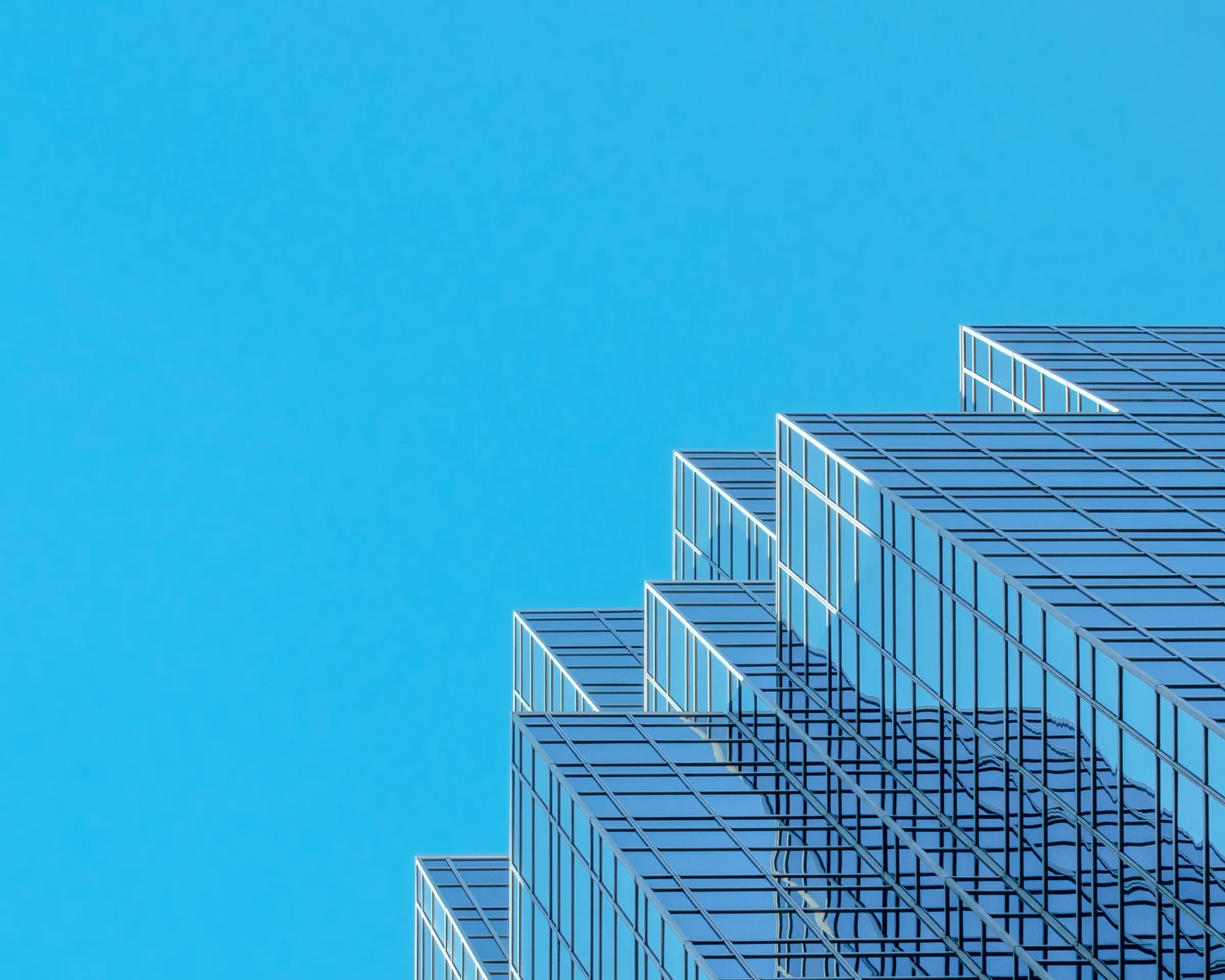 Stepped glass facade of a modern office building rising against a clear blue sky.