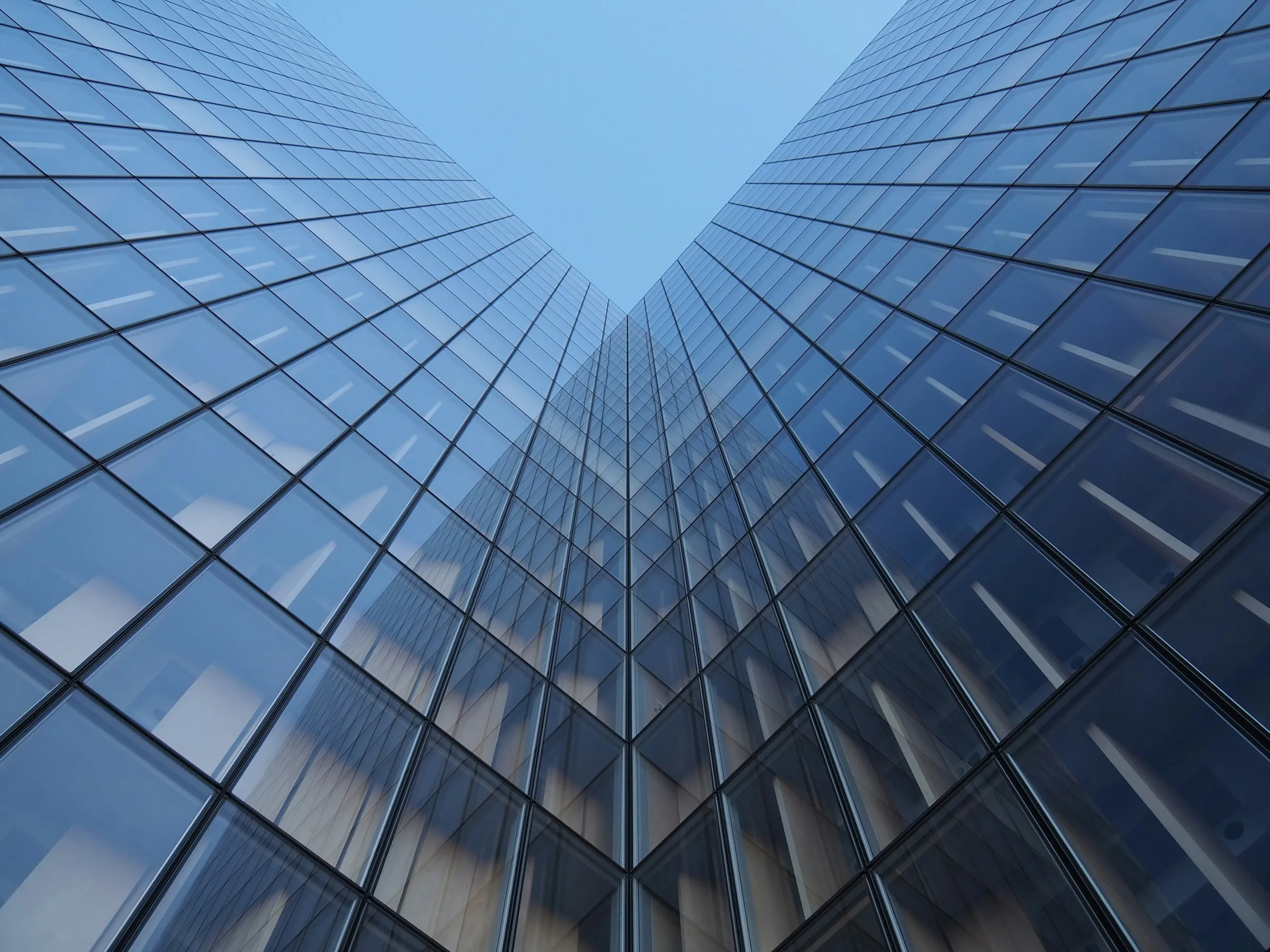 Converging glass facades of an office tower seen from below against clear sky.